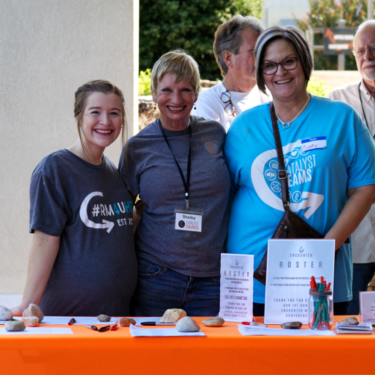 Three volunteers standing at a sign-in table.